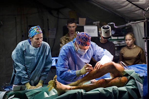 HELMAND PROVINCE, AFGHANISTAN: British Army surgeon Major Andy Bruce takes out fragments from the legs of injured British Army soldier Simon Peacock from the Royal Anglion Regiment, during surgery at the operating theatre on May 5, 2007 at the British Army Field Hospital at Camp Bastion in a location in the desert in the Helmand Province in Southern Afghanistan. Simon Peacock was injured by multiple fragments in a Taliban Rocket Propelled Grenade (RPG) attack, in which five other British soldiers were carried to the hospital with the similar injuries. The British Army hospital in Camp Bastion, run by the United Kingdom Joint Force Medical Group, provides the medical cover for all ISAF personnel operating in Helmand Province in Southern Afghanistan. In addition to the British, Danish, Estonian, Czech and American troops, who operate under the command of Task Force Helmand, the British hospital treats significant numbers of Afghan patients from across the spectrum of conflict, including Afghan National Security Forces, Taliban and civilians. The hospital, although situated in a tent, is the most advanced in southern Afghanistan. The medical team have developed groundbreaking trauma management practices including the use of consultants as part of its Medical Emergency Response Team. Early use of senior medical expertise ensures that clinical assessment can be started the moment a casualty is retrieved from the battlefield. This unique method of reducing time spent in medical reception and stabilisation has enabled patients to move from helicopter to operating table, via accident and emergency, sometimes in less than twenty minutes. The hospital boasts a five-bed accident and emergency department incorporating two portable digital x-ray machines, a CT scanner and an operating theatre where two patients can simultaneously undergo surgery. (Photo by Marco Di Lauro/Getty Images)