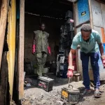 A battery breaker in Lagos, Nigeria, uses a machete to hack open the plastic casing of a car battery. (CREDIT: Grace Ekpu for The Examination)