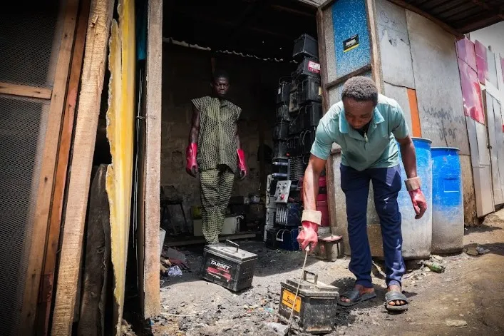 A battery breaker in Lagos, Nigeria, uses a machete to hack open the plastic casing of a car battery. (CREDIT: Grace Ekpu for The Examination)